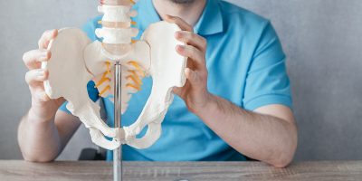 Close up of male doctor's hand showing sacroiliac joint on skeleton spine model