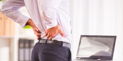 Disease back. Portrait of a businessman with a beard while working in his office, holding behind his back