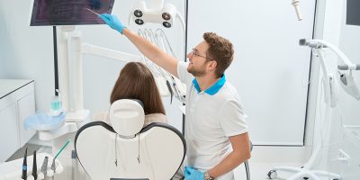 Dentist pointing at problem tooth on digital panoramic x-ray on computer screen to female client