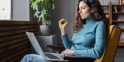 Young attractive woman employee squeezing rubber ?arpal expander in hand and looking at laptop screen during working day in modern office. Finger, hand and wrist exercises for office workers